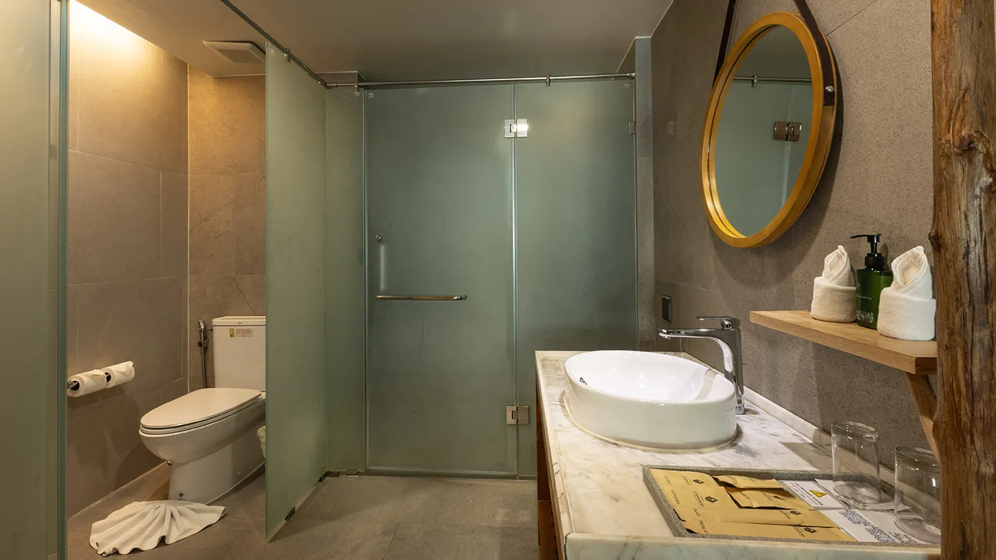 A sleek vanity with a gold-framed mirror, a glass-enclosed shower, and gray tiles accented by warm wood tones for a modern, calming feel