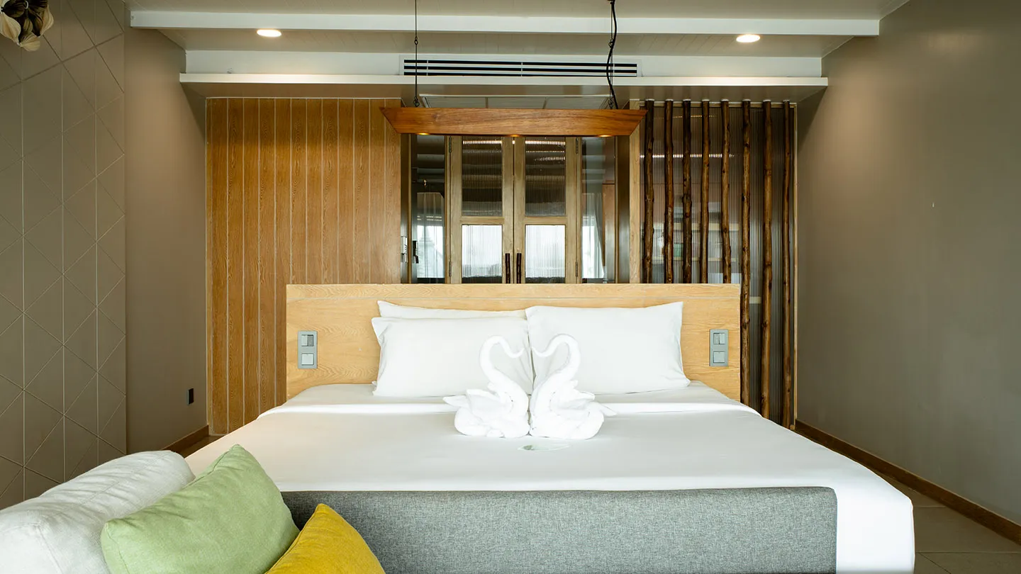 Large bed with swan towels, warm lighting, wooden furnishings, and Thai-inspired décor accented by a daybed with vibrant yellow and green cushions