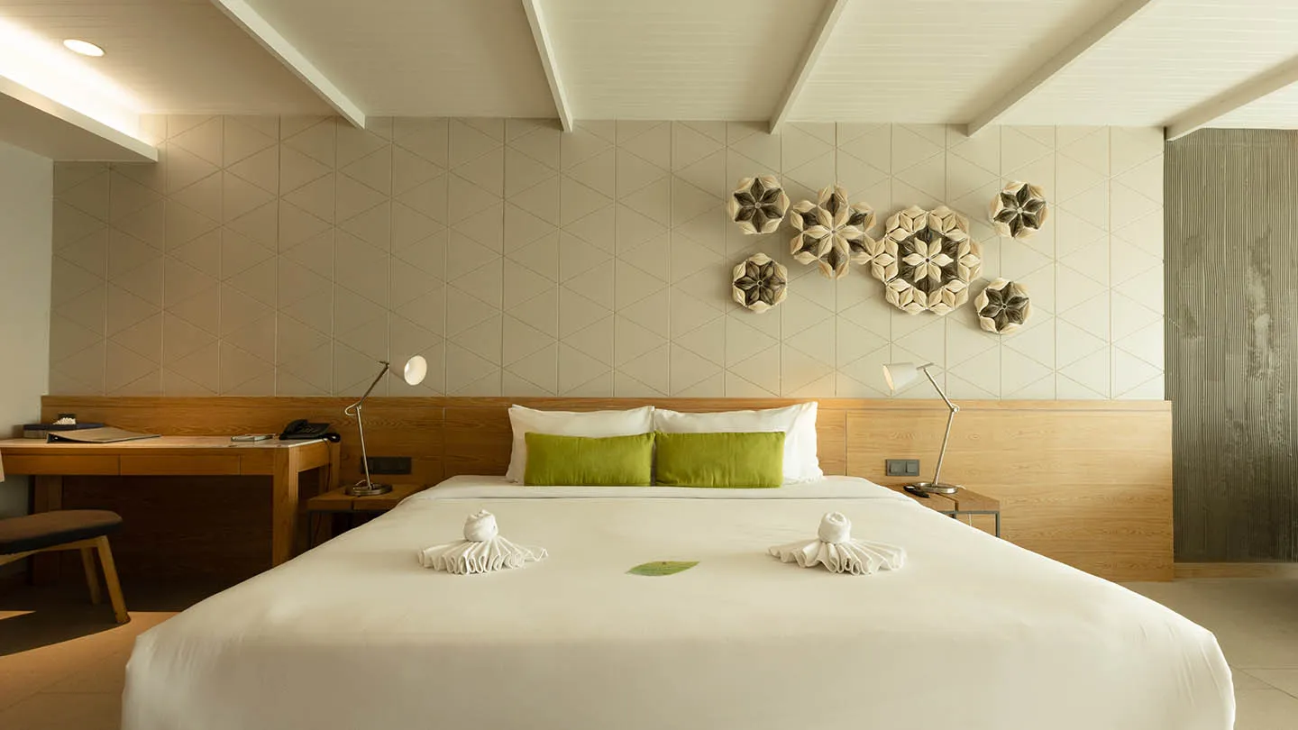 The Canna Suite features a modern, airy interior with a king-sized bed, wooden accents, refined artwork, and soft lighting, exuding comfort and calm, with views of Kata Beach and the Andaman Sea
