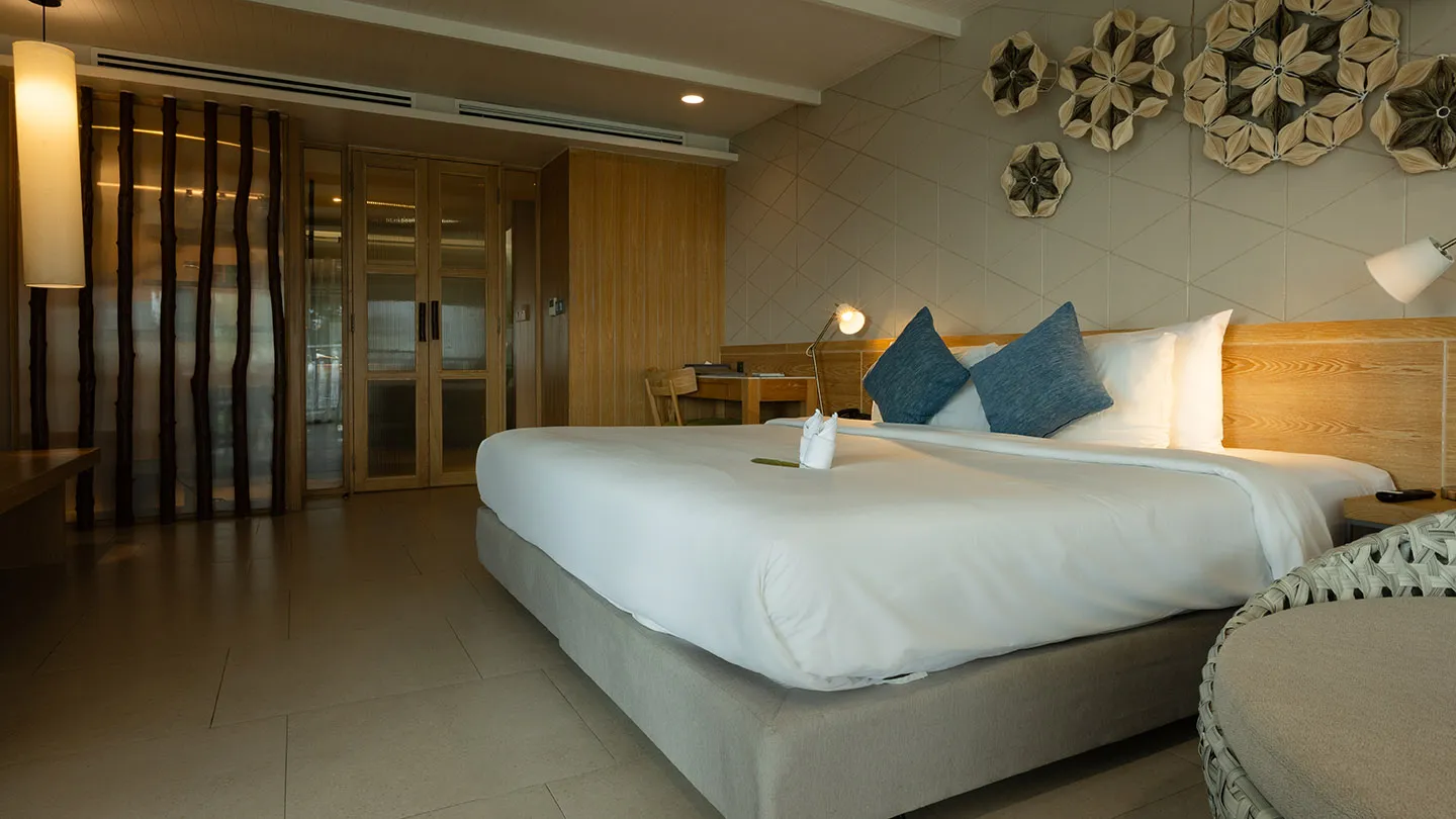 A spacious bedroom features a large bed with blue accents, a round daybed, writing desk, and modern Thai-inspired decor with warm lighting and beach resort-style details