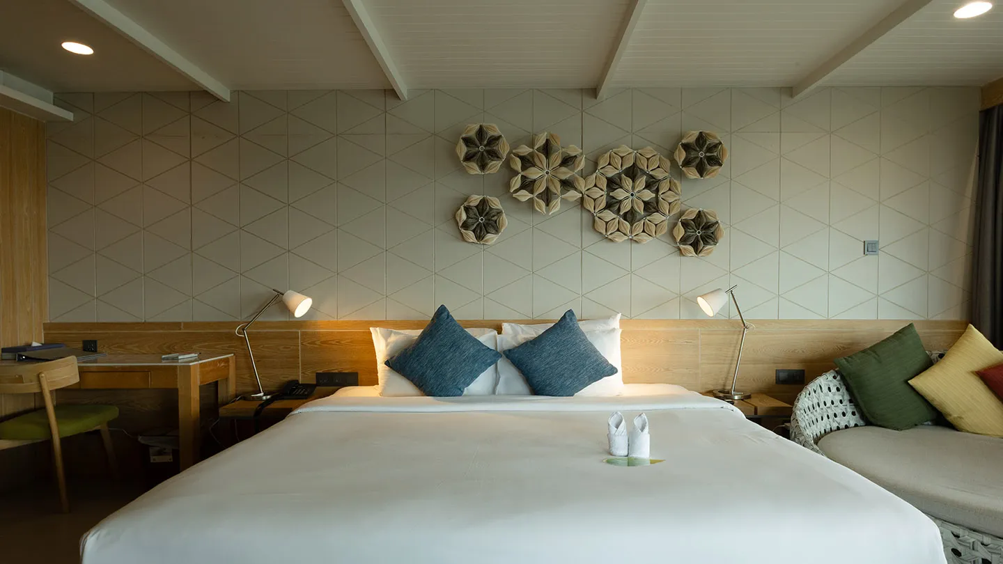 A bright, roomy suite with a large bed, contrasting pillows, bedside lamps, a desk, round daybed, and warm wooden details with star-shaped wall decor