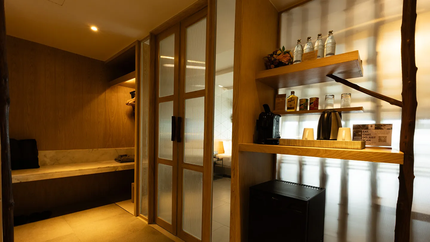 Part of the Honeymoon Suite showcases sliding wooden doors, a stylish lounge chair with a circular cushion, decorative open shelves, a floor lamp, and sunlight streaming from an adjacent outdoor space