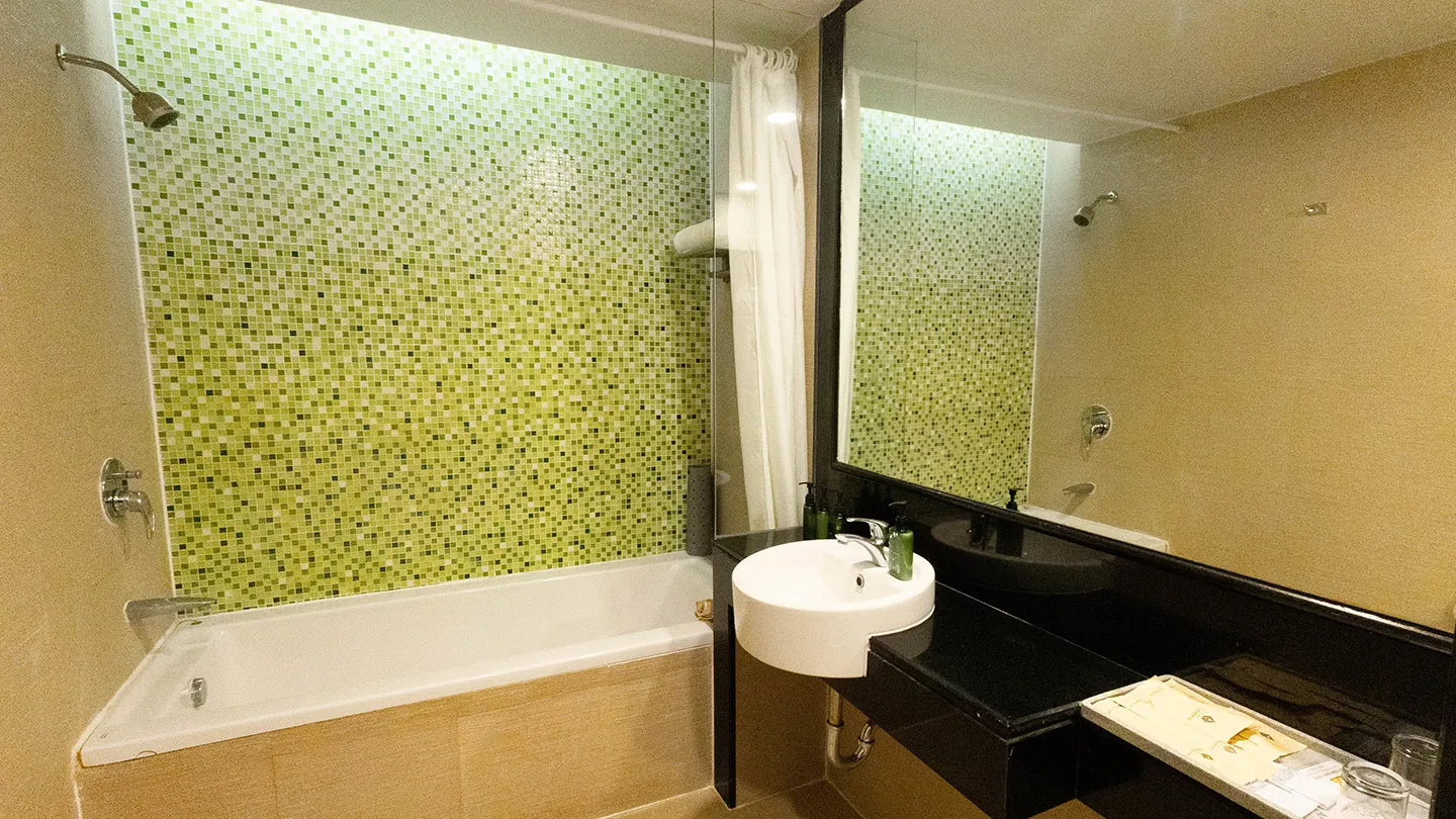 The beach hotel bathroom includes a bathtub, dark vanity with white sink, large mirror, and textured wall tiles