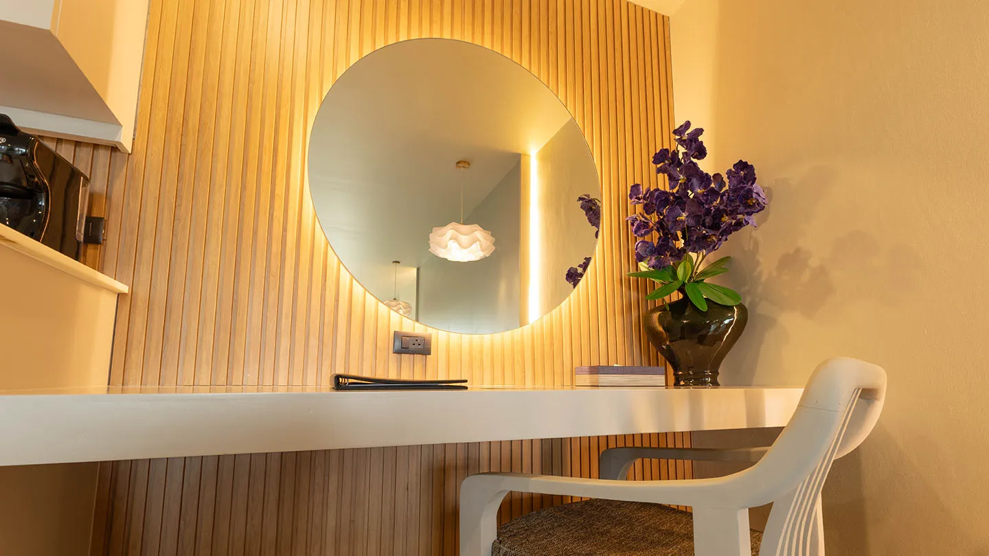 A wooden vanity paired with a backlit round mirror, a chic cushioned chair, and a tall vase of purple blooms