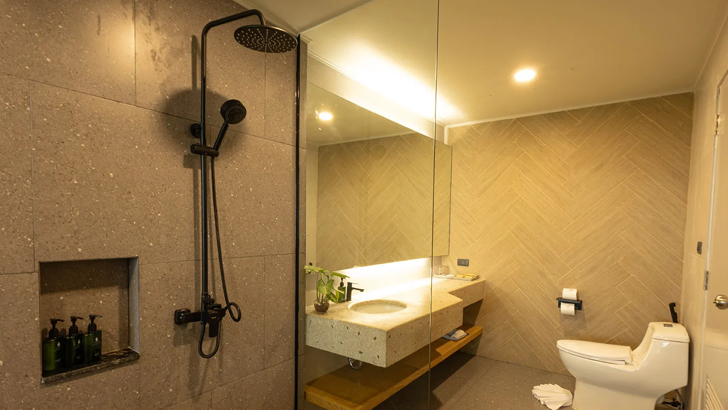 A contemporary bathroom with a walk-in shower with black fixtures, sleek vanity and mirror, white toilet, built-in shelves, and light textured tiles