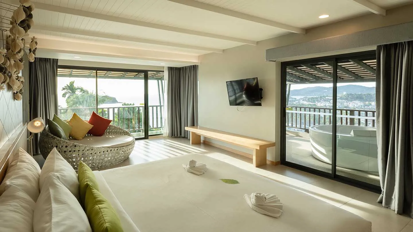 A peaceful, wood-accented bedroom leads to a private balcony with an outdoor bathtub and stunning views of Kata Beach and the Andaman Sea