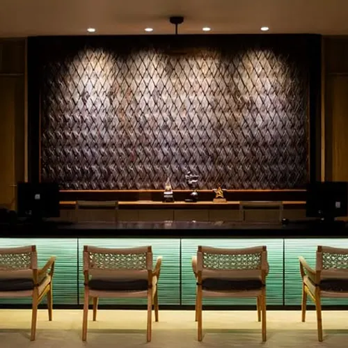 Elegant Phuket reception at Andaman Cannacia Resort with a sleek wooden front desk, woven seating, and a stylish textured wall backdrop